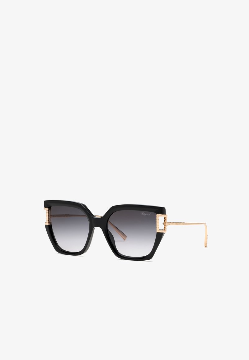 Lunettes de soleil œil de chat noires oversize avec verres dégradés et branches texturées dorées et accents près des charnières.