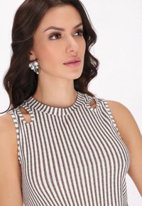 Top senza maniche con righe orizzontali bianche e marroni, con dettagli a taglio sulle spalle. La modella indossa orecchini a clip impreziositi.