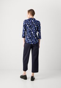 Μπλούζα με ναυτικό σχέδιο σε μπλε και λευκές αφηρημένες σχεδιάσεις; τρεις-τέταρτα μανίκια; συνδυασμένη με σκούρο παντελόνι και μαύρα παπούτσια με τακούνι.