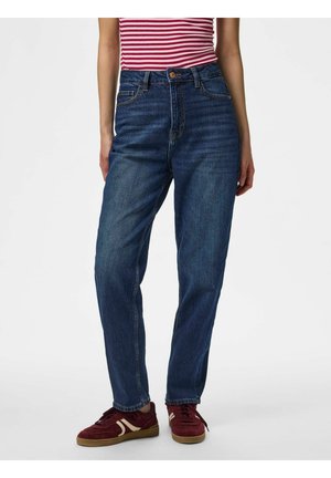 Personne portant un jean bleu taille haute jambe droite, une chemise rayée rouge et blanche et des baskets rouges avec des accents blancs, debout sur un fond blanc.