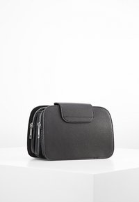 Černá kožená kabelka s texturou a klopovým uzávěrem, vybavená dvěma zipovými kapsami a obdélníkovým tvarem. Minimalistický design.