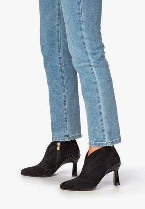 Sorte ankelstøvler i ruskind med spids tå, lynlås og en konisk hæl, parret med lyseblå straight-leg jeans.