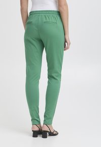 Groene, aangesloten joggers met een elastische tailleband en twee achterzakken, gecombineerd met zwarte hakken met bandjes. Glad materiaal in een effen kleur.
