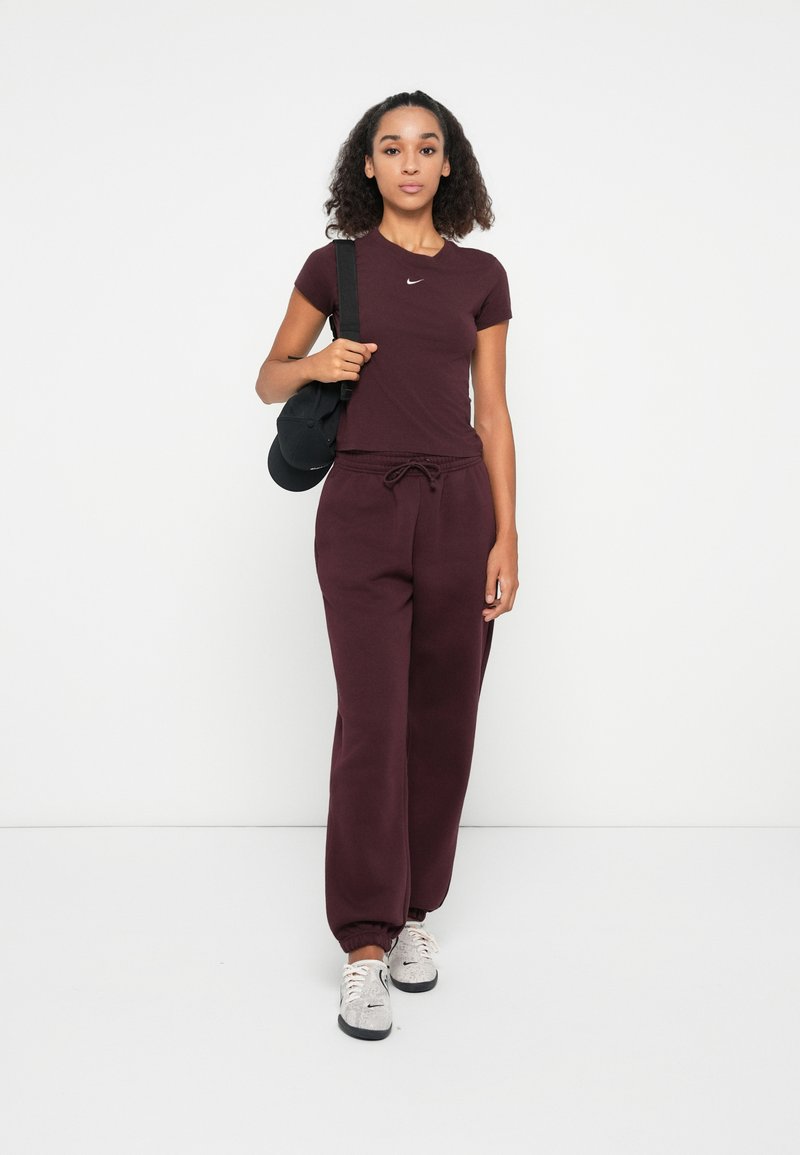 Completo sportivo color bordeaux con t-shirt a maniche corte e pantaloni della tuta abbinati. Caratterizzato da una vita con cordino e polsini elasticizzati. Sneakers grigie.