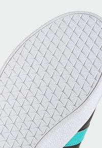 Semelle en caoutchouc blanche avec un motif diamant texturé, bords incurvés et une partie supérieure de chaussure noire et turquoise visible.