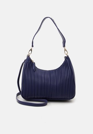 Granatowa plisowana torebka na ramię z odpinanym długim paskiem, złotymi zapięciami i zamkiem błyskawicznym na jednolitym jasnym tle.