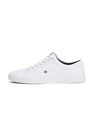 Zapatilla blanca de corte bajo con cierre de cordones, costuras mínimas y pequeño logo de bandera roja, blanca y azul en el lateral, forro interior negro.