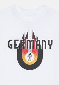 Camiseta blanca con "GERMANY" en letras negras en negrita, con un diseño en degradado de rojo, amarillo y negro debajo de un logo de Adidas y el emblema de la Euro 2024.