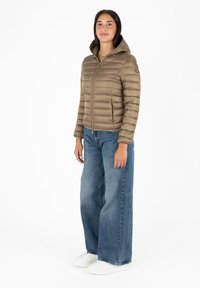 Giacca puffer khaki con motivo a righe orizzontali, chiusura con zip e cappuccio. Abbinata a jeans blu larghi e sneakers bianche.