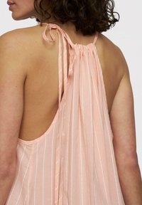 Top senza maniche di colore pesca con legature sul retro, caratterizzato da strisce bianche verticali e una silhouette fluida con un design della schiena scollato.