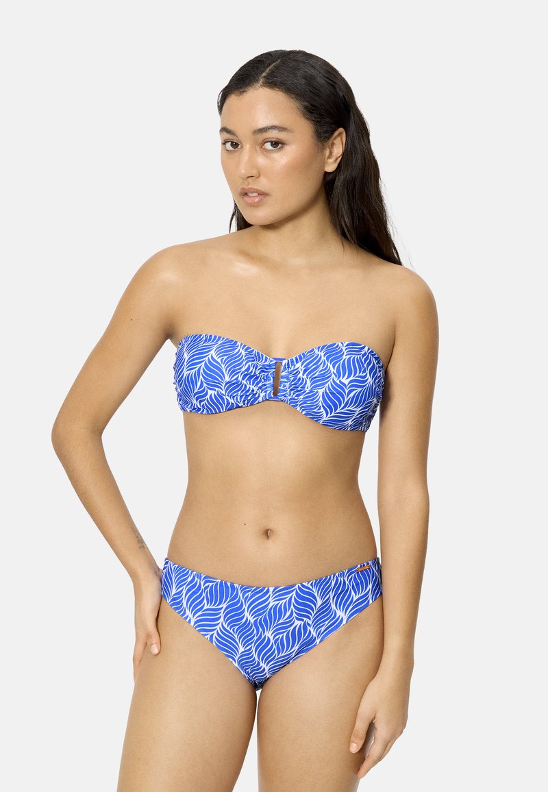 Mujer de cabello largo y oscuro, vistiendo un bikini sin tirantes azul y blanco con estampado, sobre un fondo claro y liso.