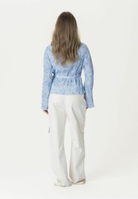 Hellblaues, long-sleeves Wickeloberteil mit strukturiertem Muster und einem Bindeband in der Taille, kombiniert mit weißen, lockeren Hosen.