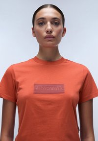 Oranges Baumwoll-T-Shirt mit einem strukturierten, rechteckigen Logo in einem dunkleren Farbton, rundem Ausschnitt und kurzen Ärmeln. Glatter Stoff, lässiges Design.