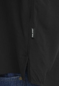 Musta lyhythihainen paita, jossa on sivuhalkio, mikä tuo esiin sujuvan tekstuurin ja pienen "BLEND"-tunnuksen helman kohdalla. Taustalla näkyy denim.