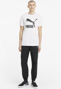 Hvid bomulds t-shirt med sort Puma-logo, parret med sorte cargo-bukser med sidelommer og elastiske manchetter samt sorte sneakers.