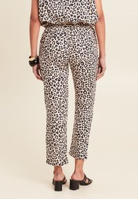 Leopardenprint broek met een beige achtergrond, recht model, elastische tailleband en contrasterende zwarte patronen. Draagt met haksandalen.