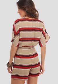 Jumpsuit de manga corta en beige con rayas rojas y negras. Presenta una cintura ceñida y un escote redondo con un cierre de botón en la parte posterior.