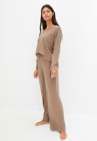 Ensemble de détente à côtes marron comprenant un haut à manches longues ample et un pantalon à jambes larges. Le haut a un col en V et un détail à nouer à la taille.