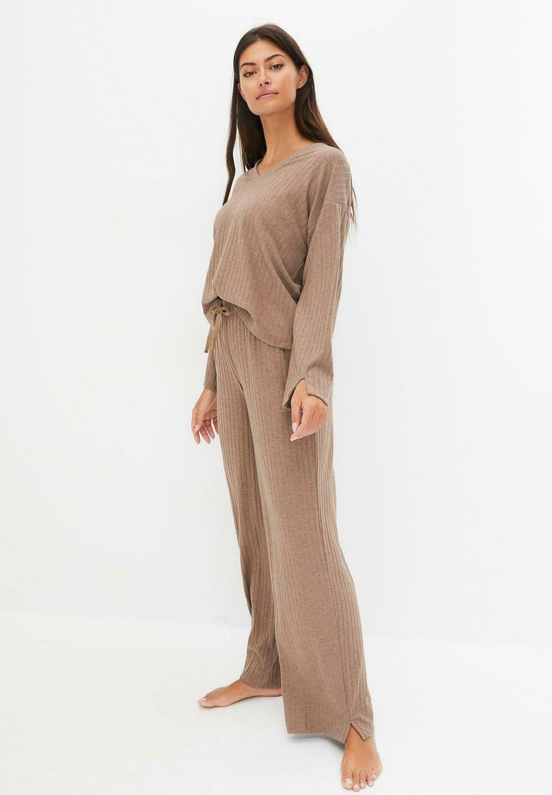 Ensemble de détente à côtes marron comprenant un haut à manches longues ample et un pantalon à jambes larges. Le haut a un col en V et un détail à nouer à la taille.