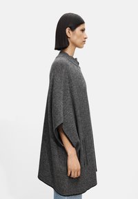 Overdimensjonert, grå strikket poncho med rund krage, sidespalter og ermer som går til albuen. Myk tekstur med løs og avslappet passform.