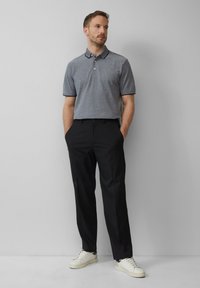 Grijze polo met een contrasterende marineblauwe kraag, zwarte op maat gemaakte broek en witte sneakers. De stof lijkt soepel; de pasvorm is ontspannen maar gestructureerd.