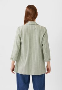 Hellgrünes gestreiftes Blazer mit Reverskragen, Dreiviertelärmeln und Knopfdetails, kombiniert mit dunkelblauen Jeans. Glatte Textur.