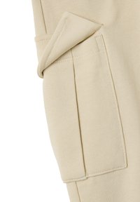 Tejido de algodón beige con detalle de bolsillo doblado, que presenta un acabado de costura limpio y una textura suave. Ideal para ropa casual.