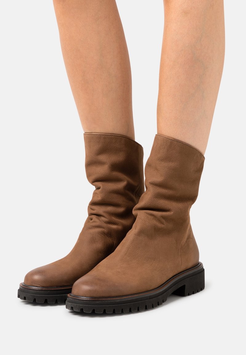 Bottines marron en cuir souple avec une finition mate, un bout rond et une semelle épaisse en caoutchouc noir avec des rainures texturées.