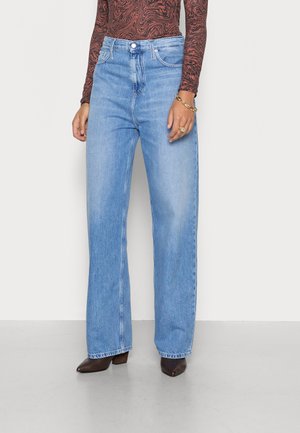 Jeans a gamba larga blu chiaro in denim. Caratterizzati da una vita alta, chiusura fronte a bottoni e una leggera scoloritura. Indossati con scarpe con tacco a punta marroni.