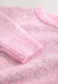 Ružový vlnenný sveter s jemnou, mäkkou chlpatou textúrou. Má rebrované manžety a okrúhly výstrih, s jemnými viacfarebnými škvrnami po celej ploche.
