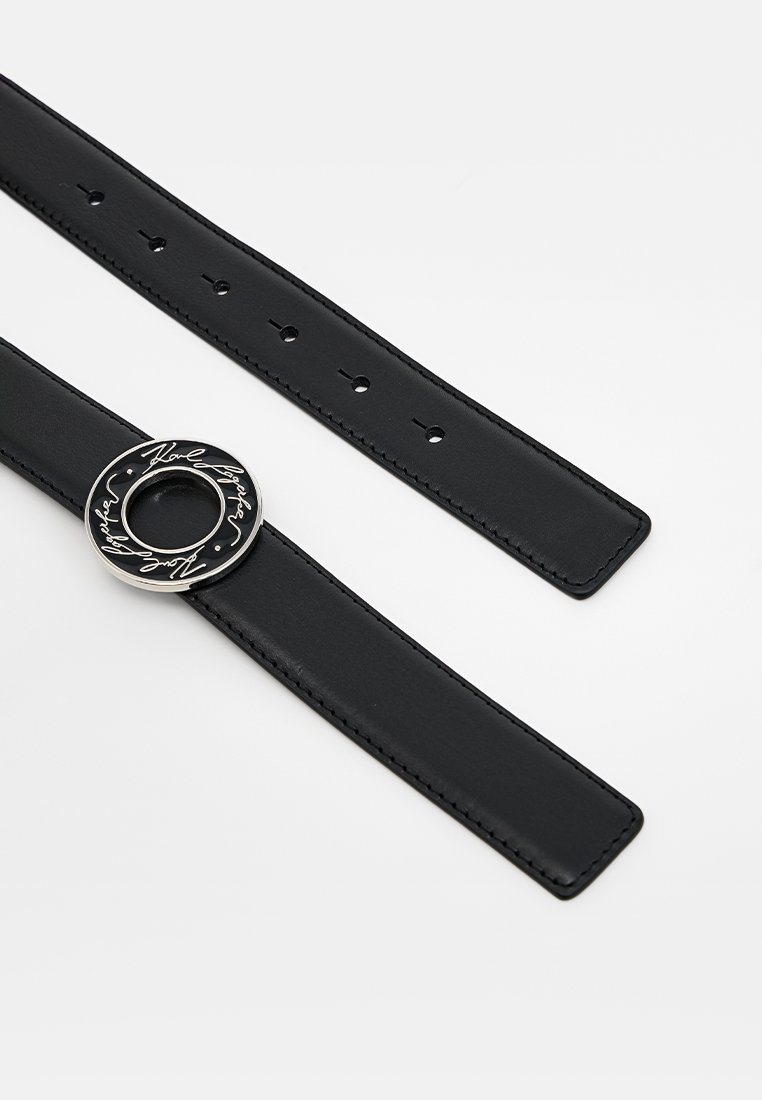 Ceinture en cuir noir, design plat, réglable avec des trous. Elle dispose d'une boucle en métal ronde avec une inscription embossée et une découpe centrale.
