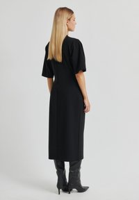 Robe noire à silhouette ajustée, manches courtes ballon et ourlet droit. Portée avec des bottes noires montantes jusqu'aux genoux. Texture lisse.