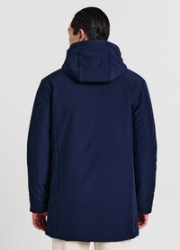Parka blu navy con cappuccio, caratterizzata da una texture liscia e un design semplice. Le maniche sono aderenti e la lunghezza arriva a metà coscia.