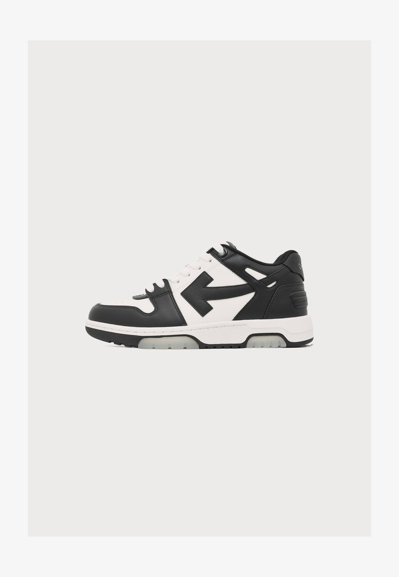 Ασπρόμαυρο χαμηλό sneaker με λευκά κορδόνια και μαύρη λεπτομέρεια βέλους στο πλάι, πάνω σε απλό ανοιχτό φόντο.