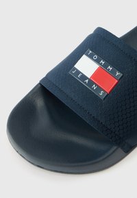 Cipele za klizanje u mornarsko plavoj boji s teksturiranom trakastom trakom, sa pravokutnim logotipom u crvenoj, bijeloj i plavoj boji. Glatka crna potplat za udobnost.