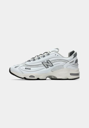 Weißer Sport Sneaker mit grauen Akzenten, aus Mesh- und synthetischen Materialien, Wellenmuster, gepolstertem Schaft und Gummisohle mit schwarzem Profil.