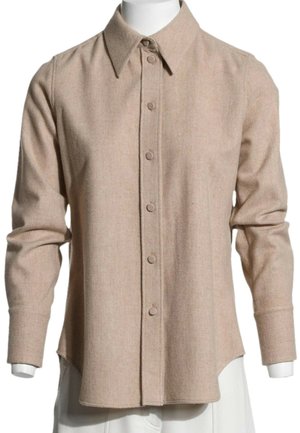 Langærmet beige skjorte med knapper og spids krave vist på en hvid mannequin krop.