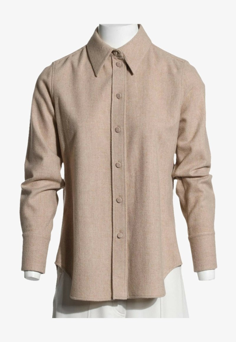 Chemise beige à manches longues boutonnée avec col pointu exposée sur un torse de mannequin blanc.