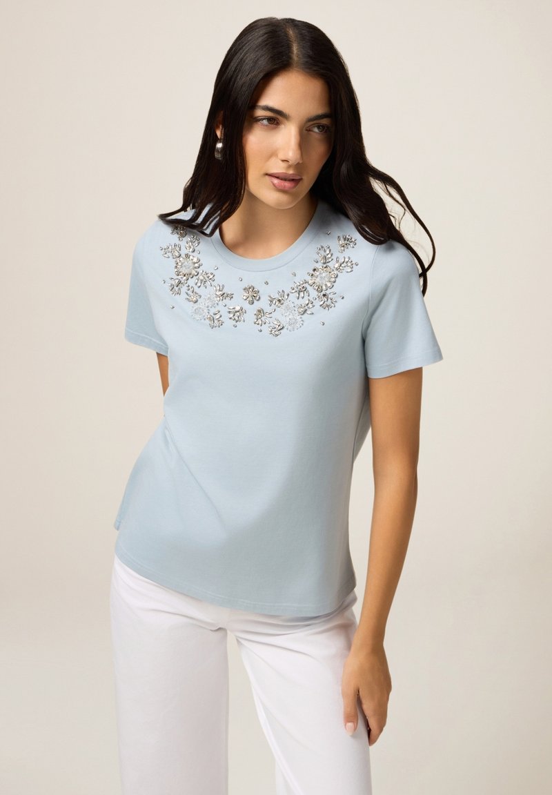 T-shirt bleu clair à manches courtes avec broderies florales et ornements autour de l'encolure. Matière en coton lisse, coupe décontractée.