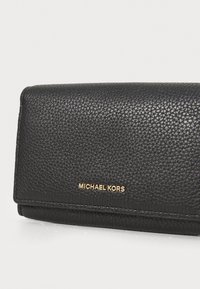 Black leather wallet with a textured surface, featuring a gold "MICHAEL KORS" logo on the front, and a flap closure. Compact design.