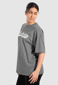 Grå oversized t-shirt lavet af bomuldsblanding, med en tydelig hvide skriftlogo på brystet og korte ærmer.