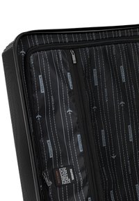 Intérieur d'une valise rigide noire, avec un revêtement texturé présentant des motifs alternés de logos et d'illustrations d'avions, comprenant des poches zippées.