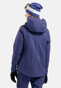 Wasserdichte marineblaue Skijacke mit Kapuze, mit glatter Textur und verstellbarem Saum, kombiniert mit einer blauen Mütze und Skibrille.