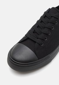 Svart kanvas sneakers med gummitå och texturerad gummisula. Har platta skosnören och metallöglor för säker fastsättning.