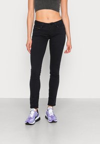 Svarta slim fit jeans med en jämn yta, med en midjehöjd av medelhöjd och standardfickor, i kombination med lila och vita sneakers.