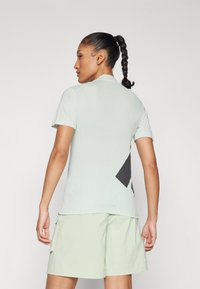 Šviesiai žalia trumpomis rankovėmis polo marškinėliai su tinklo nugarą ir juodais geometriniais raštais. Dėvimi su derančiais šviesiai žaliais šortais, turinčiais šonines kišenes.