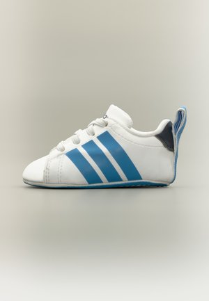 Chaussure bébé blanche avec des rayures bleues, des lacets blancs et un passant au talon rayé bleu, vue de côté sur un fond neutre.
