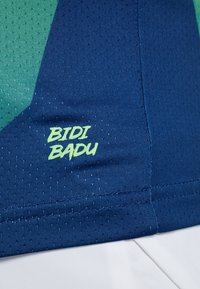 Modrá sportovní látka s texturovaným povrchem. Obsahuje zelený geometrický design a logo "BIDI BADU" v jasně zelené barvě na bočním švu.