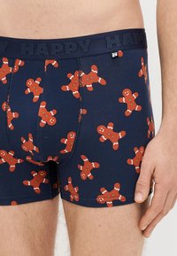 Cuecas tipo boxers azul-marinho com padrão de biscoitos de gengibre vermelhos decorados com glacê branco. Cintura elástica com a etiqueta "HAPPY". Textura de tecido macio.