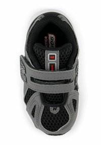 Chaussure de sport noire et grise avec tige en maille, sangles Velcro, collier rembourré et semelle extérieure blanche. Comprend le logo "NB" et des accents en caoutchouc.